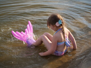 Dziewczynka przebrana za syrenkę siedzi na brzegu jeziora