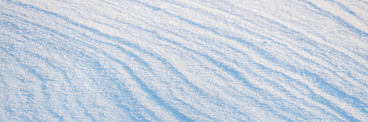 Beautiful winter background with snowy ground. Natural snow texture. Wind sculpted patterns on snow surface. Wide panoramic texture for background and design.