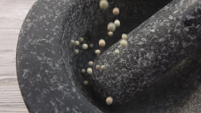 Close-up of spicy white peppercorns falling into the grey stone mortar in slow motion