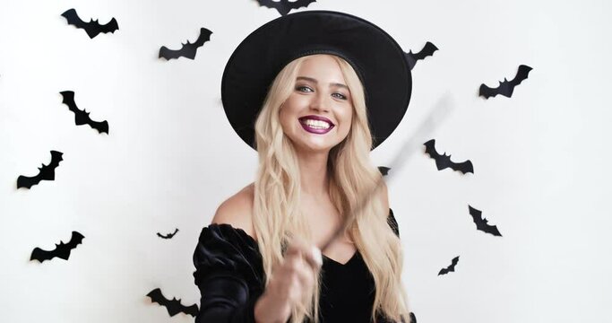 Hocus pocus. Cheerful Halloween witch gesturing with magic wand at camera, making miracle
