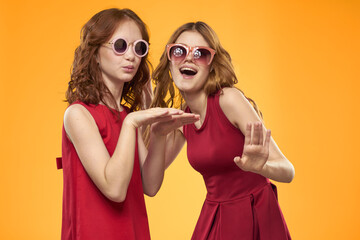 Happy sisters in red dresses on a yellow background are having fun and gesticulating Copy Space