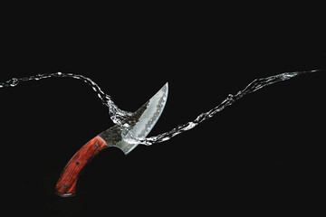 Damascus steel knife cuts water on a black background. High quality photo - obrazy, fototapety, plakaty