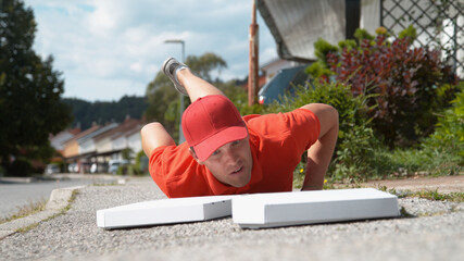 CLOSE UP: Uncoordinated delivery man falls to the ground and drops two pizzas. - obrazy, fototapety, plakaty