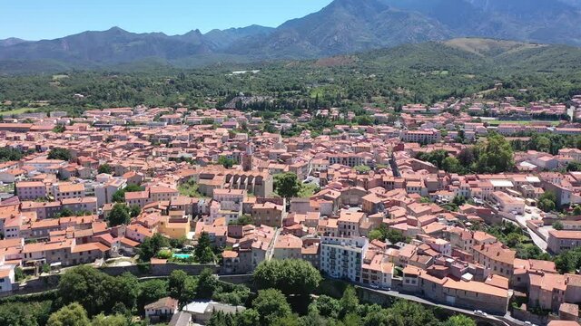 Scenic drone view of Prades summer cityscape surrounded by mountains overlooking bell tower of Saint-Pierre Church, Pyrenees-Orientales, France