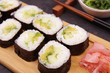 Japanese Maki rolls with cucumber and avocado on a wooden tray, served with ginger, soy sauce and seaweed salad.  