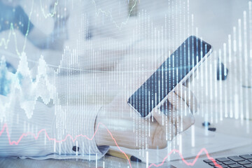 Double exposure of man's hands holding and using a digital device and forex graph drawing. Financial market concept.