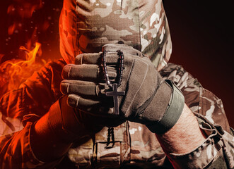 Photo of a military soldier in uniform and armor helmet sitting and holding cross religious...