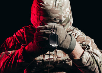 Photo of a military soldier in uniform and armor helmet sitting and holding metal army necklace on...