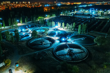 Aerial night view of modern wastewater treatment plant with round pools for cleaning sewage, drone...