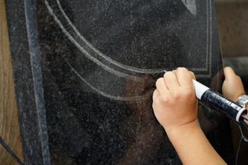 Female hand engraves black granite with an electric drill.