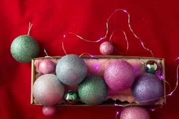 christmas balls lie in a box on a red background with a pink garland.new year, merry christmas
