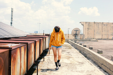 Soft focus photo of Short hair woman walking looking down wearing yellow hoodie, short denim pants and sneakers on daylight at building rooftop