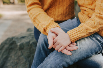 adult and child in the same yellow knitted sweaters and blue jeans hold hands tightly, faceless trend, family care