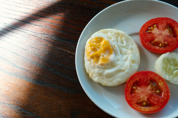 Fried egg served with slice fresh tomato and cucumber on white plate and wooden table