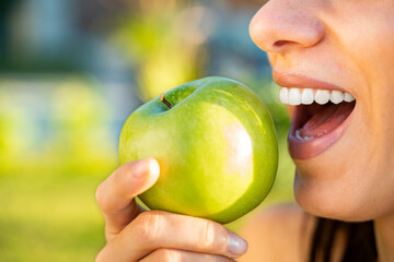 Closeup shot of young woman with perfect teeth biting green apple 