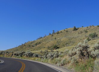 Sloping hills with sparse vegetation along a paved road at Yellowstone National Park heading toward Gardiner, Montana.