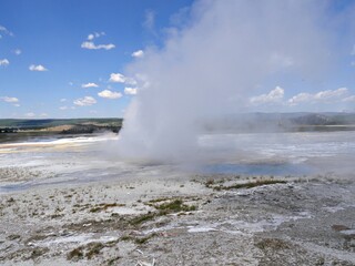 Wide shot of Clepsydra Geyser with steam shooting up at the Lower Geyser Basin, Yellowstone National Park.