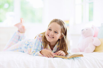 Child reading book in bed. Kids read in bedroom.