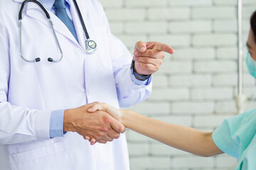 Doctor and woman patient making a handshake and doctor pointing a forefinger to patient. Trust in medication and health care service concept. Expertise specialist doctor giving a recommendation.