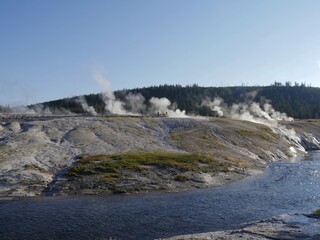 Wyoming, USA--July 2018: Erupting geysers and running streams of hot water, with people in the boardwalks at the Upper Geyser Basin, Yellowstone National Park in Wyoming.