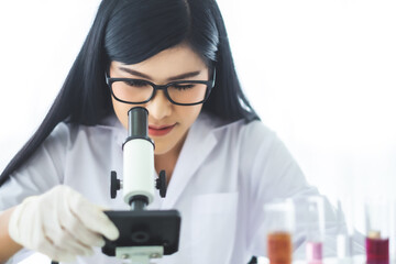 Young Asian scientist woman looking through a microscope in a laboratory