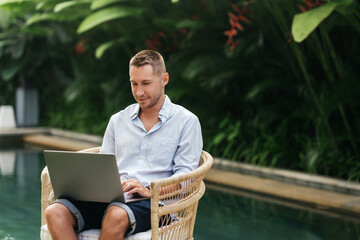 Young man using a laptop computer in a garden with a swimming pool. business, study, freelance