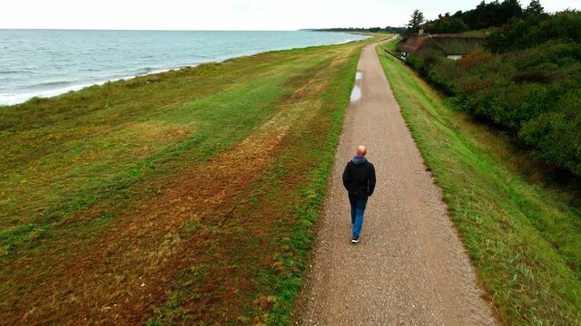 Man walking alone on a path along the coast on a windy autumns day.