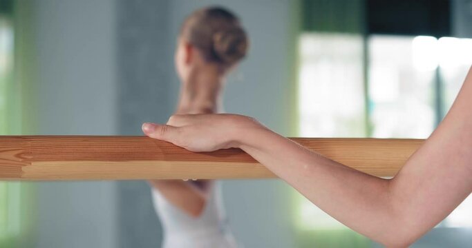 Preteen ballerina hand on barre and girl with bun doing exercise blurry reflection in mirror at lesson closeup slow motion