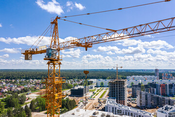 modern apartment buildings complex under construction. yellow building cranes on construction site against blue sky background. aerial photography