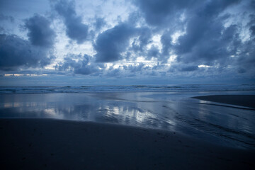 Wide area of water on the sand reflecting a dark moody sky