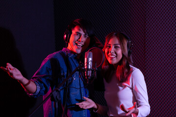 Portrait of asian young woman and man, artist singing into a microphone while recording a song in a studio