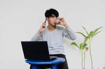 Asian young man sitting in front of the laptop drinking coffee