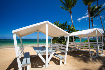 Close up view of wooden white pergola with table and benches on the paradise beach cafe with palm...