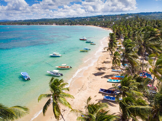 Aerial drone panoramic view of the paradise beach with sandy shore, coral spots, palm trees, color boats and blue water of Atlantic Ocean, Las Terrenas, Samana, Dominican Republic - obrazy, fototapety, plakaty