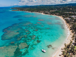 Fototapeta na wymiar Aerial drone panoramic view of the paradise beach with sandy shore, coral spots, palm trees, color boats and blue water of Atlantic Ocean, Las Terrenas, Samana, Dominican Republic