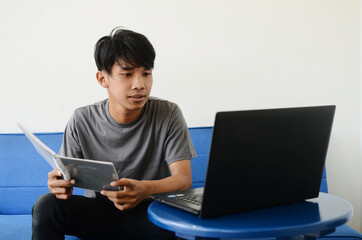 The Asian man was sitting on the sofa busy with his work