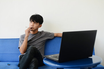 Asian man wearing ash shirt smokes on sofa