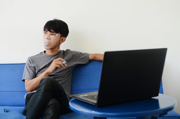 Asian man wearing ash shirt smokes on sofa