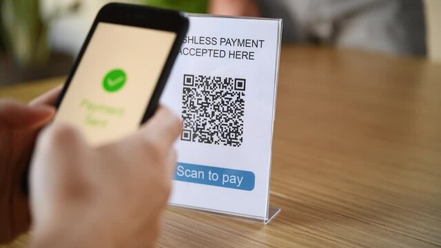 Close up hands of woman making a quick and easy contactless payment with her smartphone in a cafe. Girl scanning barcode for contactless payment in the cafe with mobile. 