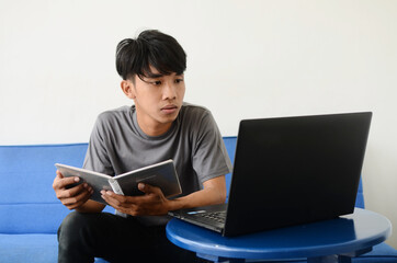 a young Asian man sitting on the sofa staring at the laptop