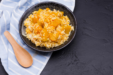 Rice with pumpkin curry in a black ceramic bowl, placed on a black table, top view.