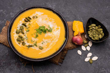 Curry or pumpkin soup with rice served in a ceramic platter on a black background - top view with writing space.