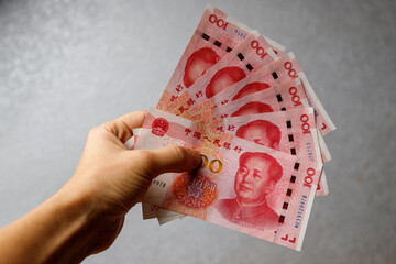 Hand holding one hundred Yuan notes against gray background