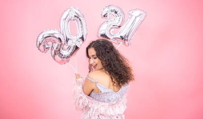 Girl on a pink background with silver balloons from the numbers 2021 in her hands