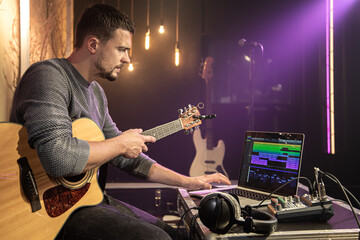 Obraz premium A male guitarist is recording a new song in a music studio using a special program on his laptop. Musical creativity concept.