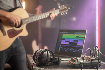 Obraz na płótnie Canvas Professional headphones connected to a music mixer and laptop. Against the background, a male guitarist in the process of recording music.