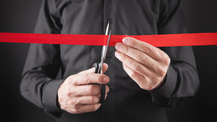Man cutting red ribbon with a scissors.