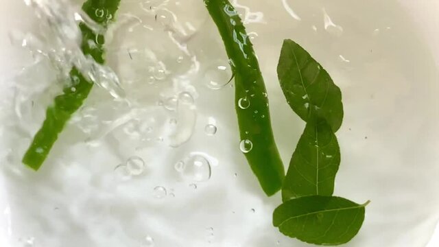 Pouring water into a bowl with leaves and green chilies as eggplant or aubergine and onions are dropped creating beautiful splashes bubbles and ripples - Powered by Adobe