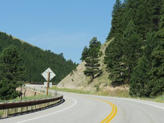 Scenic road twisting around mountainsides with protective rail fence at Bighorn National Forest in northern Wyoming.