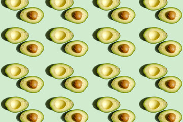 Fruit pattern. Repetition of whole and half avocado on light green background.Beautiful fruit pattern from natural fruits. Horizontal. The concept of healthy food and vegetarianism.